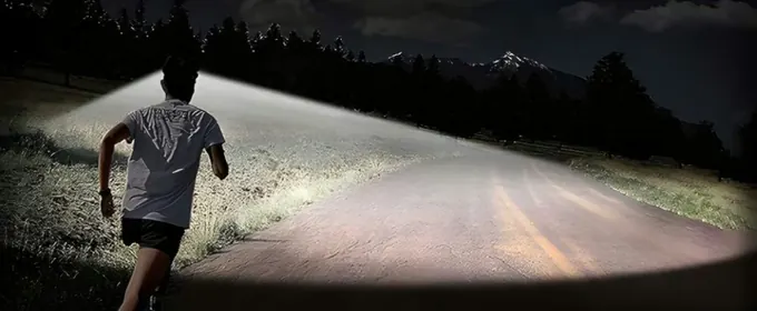 Runner on a dark country road with a wide pool of headlamp light ahead